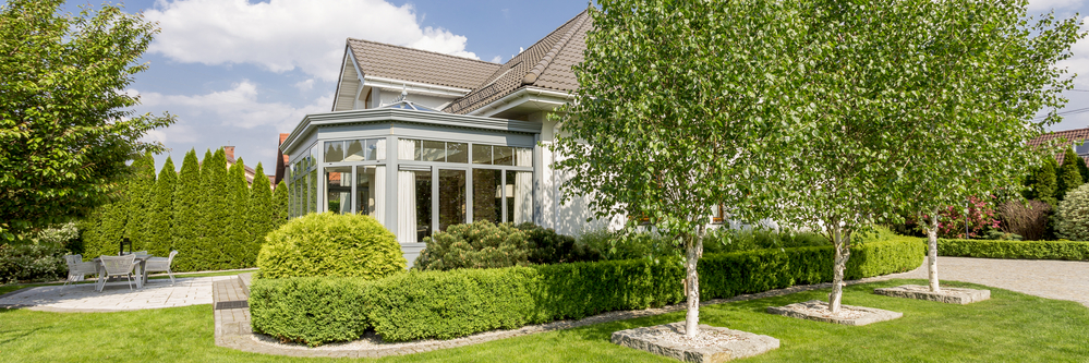 House exterior with elegant orangery in well-kept and green garden with a terrace and trees